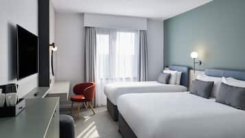 Une chambre d’hôtel avec un lit, un bureau avec une télévision, une chaise et une fenêtre avec des rideaux.