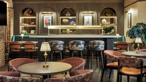 A bar area with multiple seating options, including round tables and cushioned chairs, with a decorative backdrop and wall-mounted shelves. - Leonardo Hotel Dublin Parnell Street (Dublin)