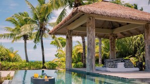 A poolside area with a thatched-roof structure, lounge chairs, and a small boat.