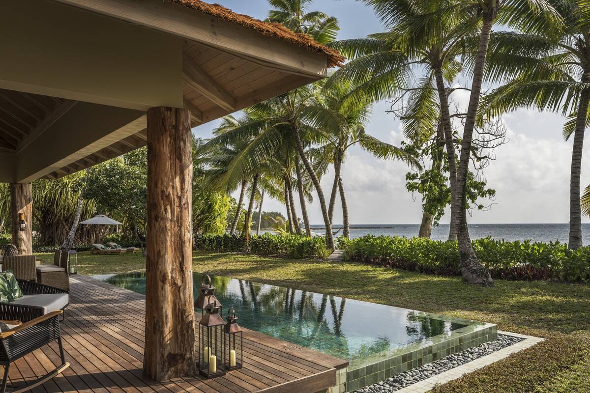 Un área junto a la piscina con sillones reclinables, una terraza de madera y vistas al océano.