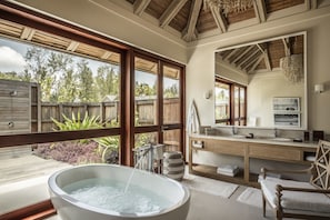A spacious bathroom with a large bathtub, wooden accents, a wooden vanity, and a large mirror.