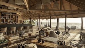 A beachside bar with wooden furniture and hanging lights, overlooking the ocean.