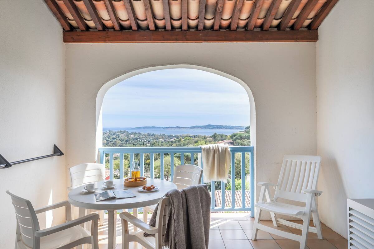 A balcony with a table, chairs, and a view of the sea.