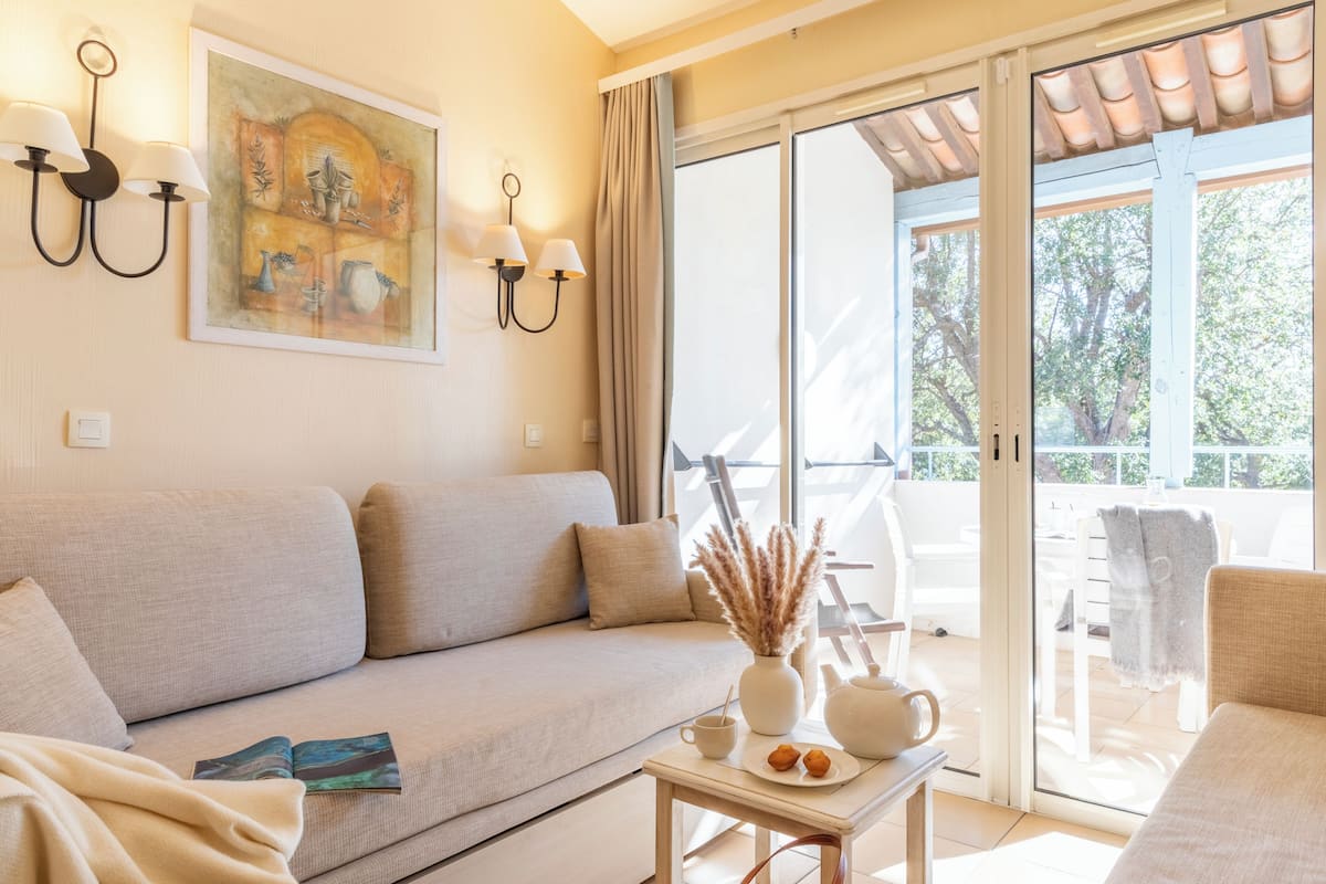 A living room with a sofa, a table with a vase and a book, and a sliding glass door leading to an outdoor area.