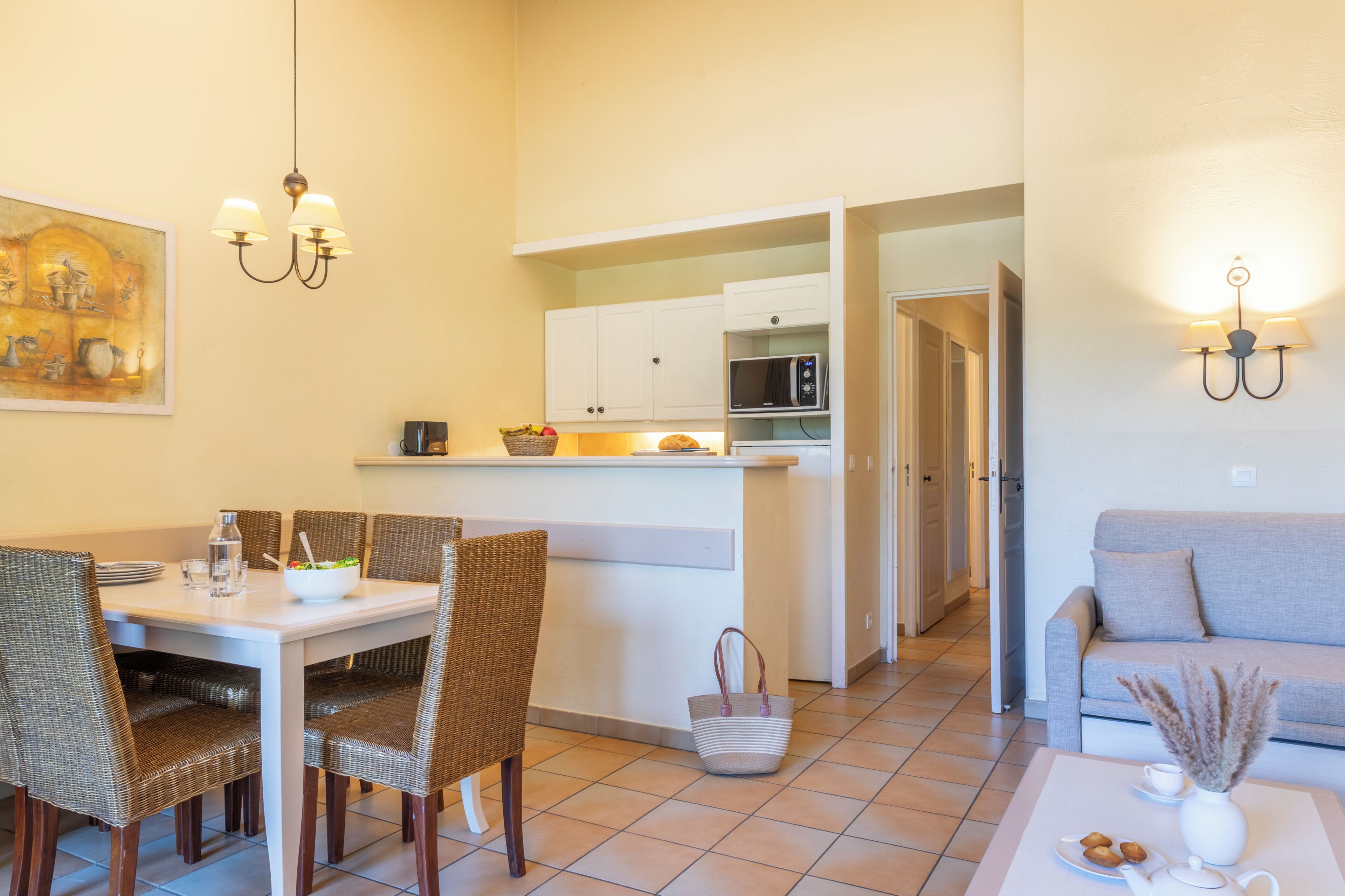 Een eetgedeelte met rieten stoelen, een witte tafel en een keuken op de achtergrond.