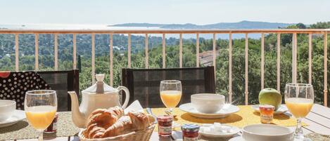 Una mesa de desayuno con cruasanes, zumo de naranja y vistas a un paisaje boscoso.