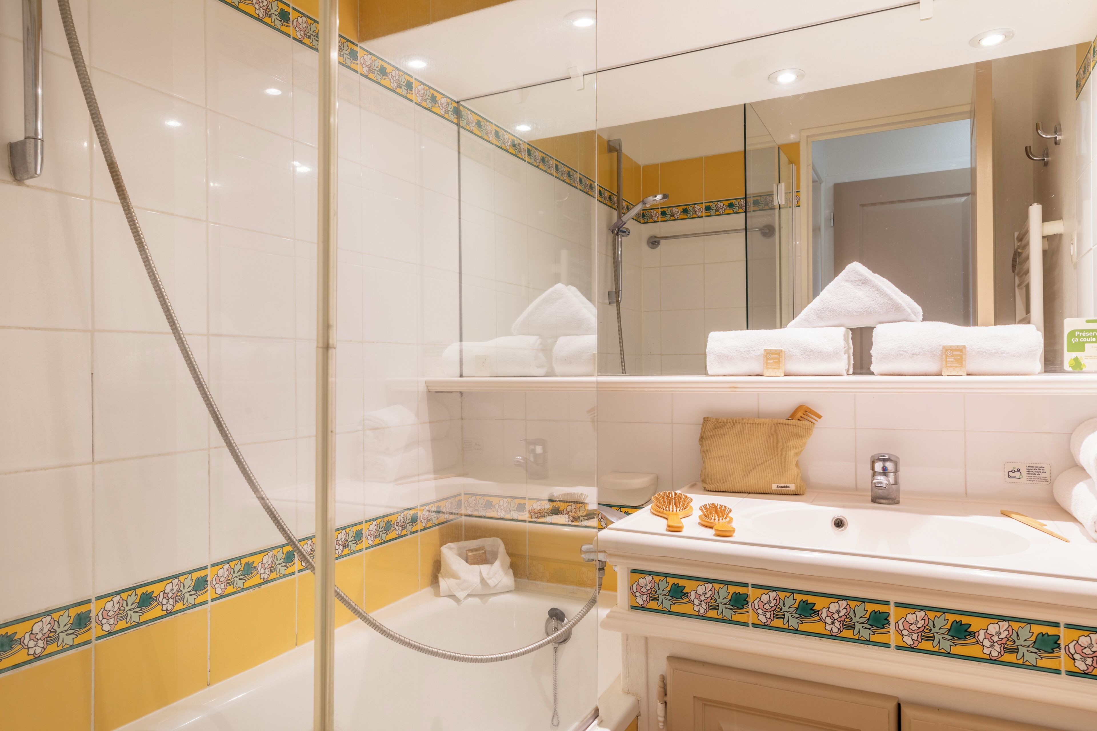 Een badkamer met een douchecabine van glas, een wastafel met toiletartikelen en een spiegel.