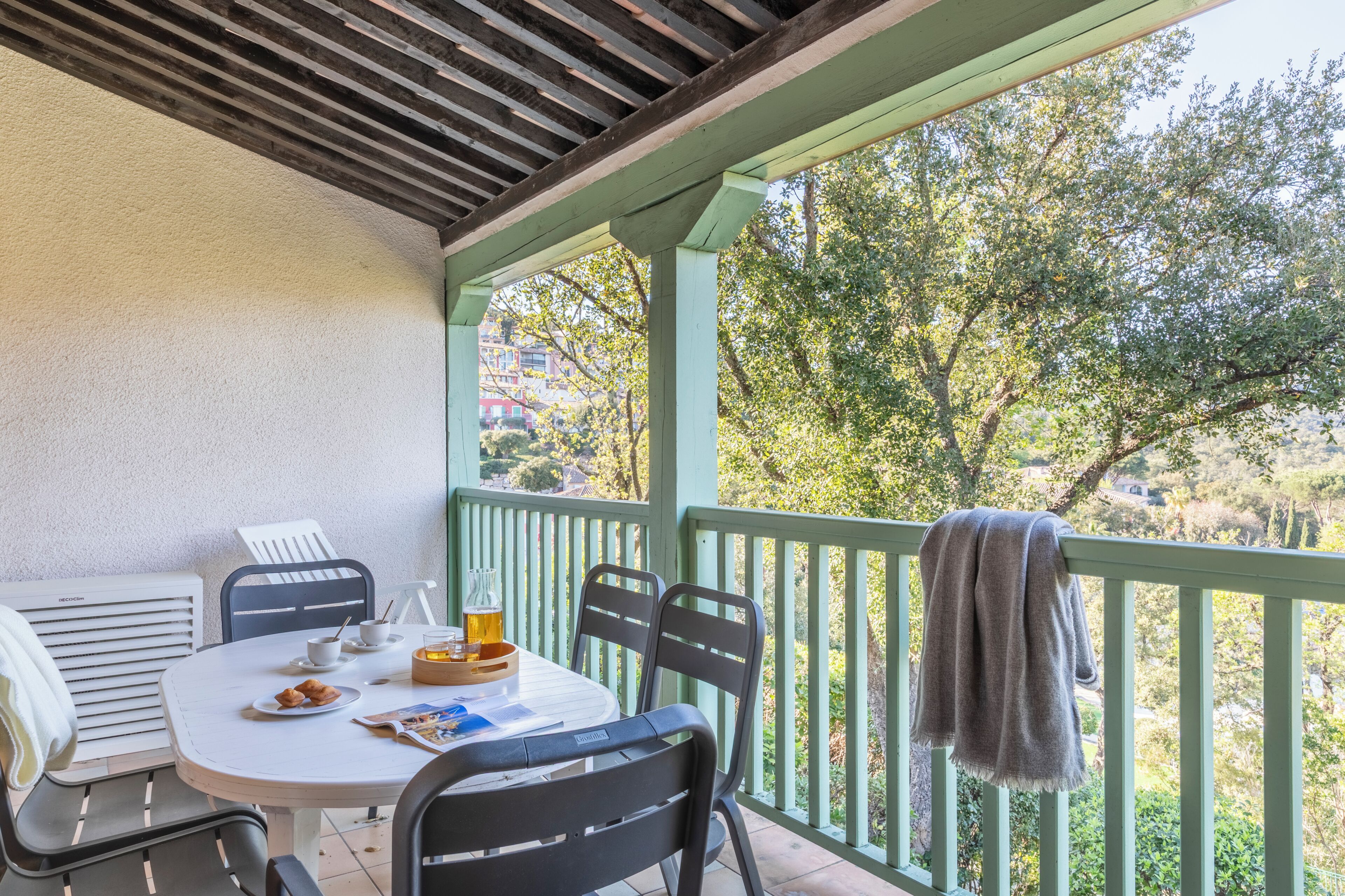 A covered outdoor dining area with a table, chairs, and a view of trees and buildings.