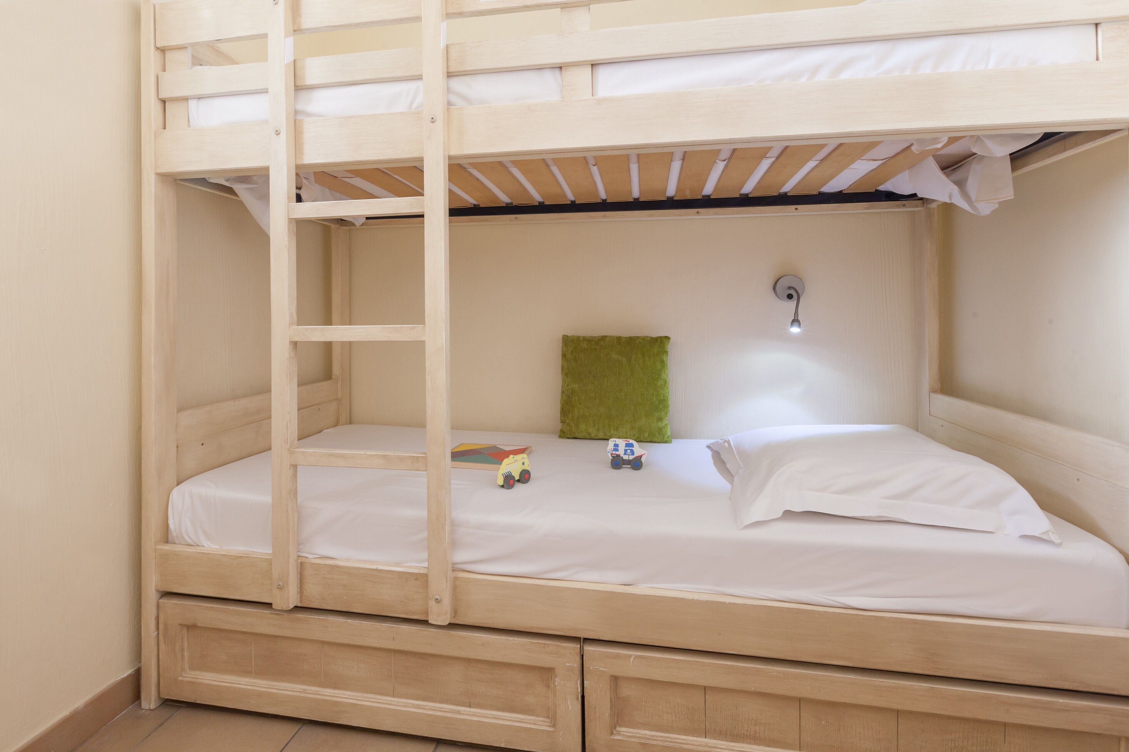 Een stapelbed met een ladder, een groen kussen en twee speelgoedauto's op de matras.