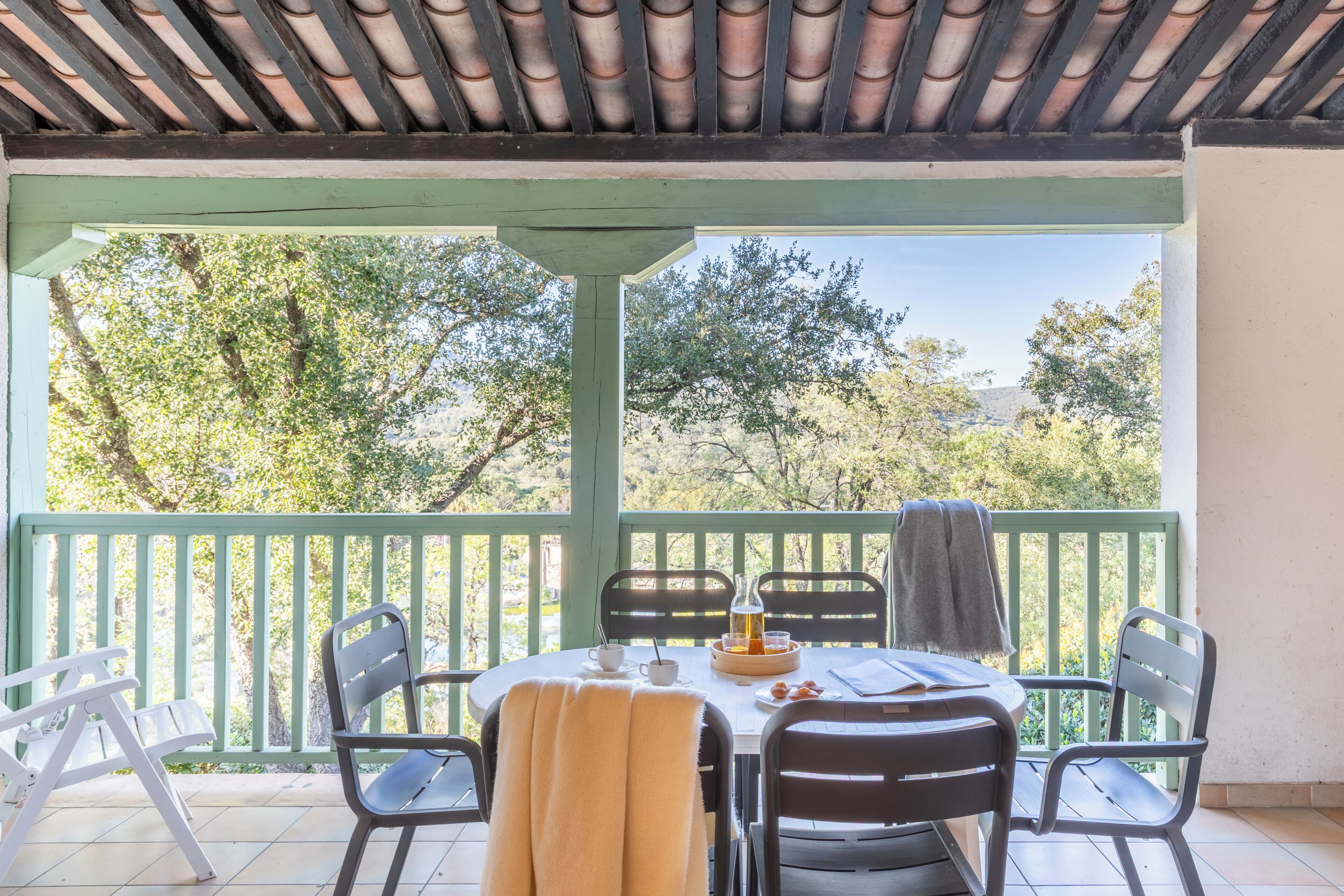 Un espace extérieur abrité, aménagé pour prendre les repas, avec une table, des chaises et une vue sur les arbres.