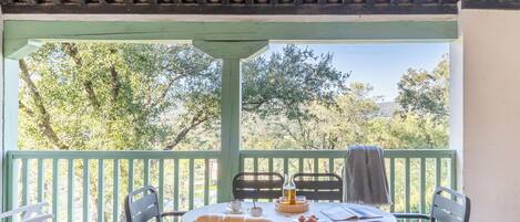 Un espace extérieur abrité, aménagé pour prendre les repas, avec une table, des chaises et une vue sur les arbres.