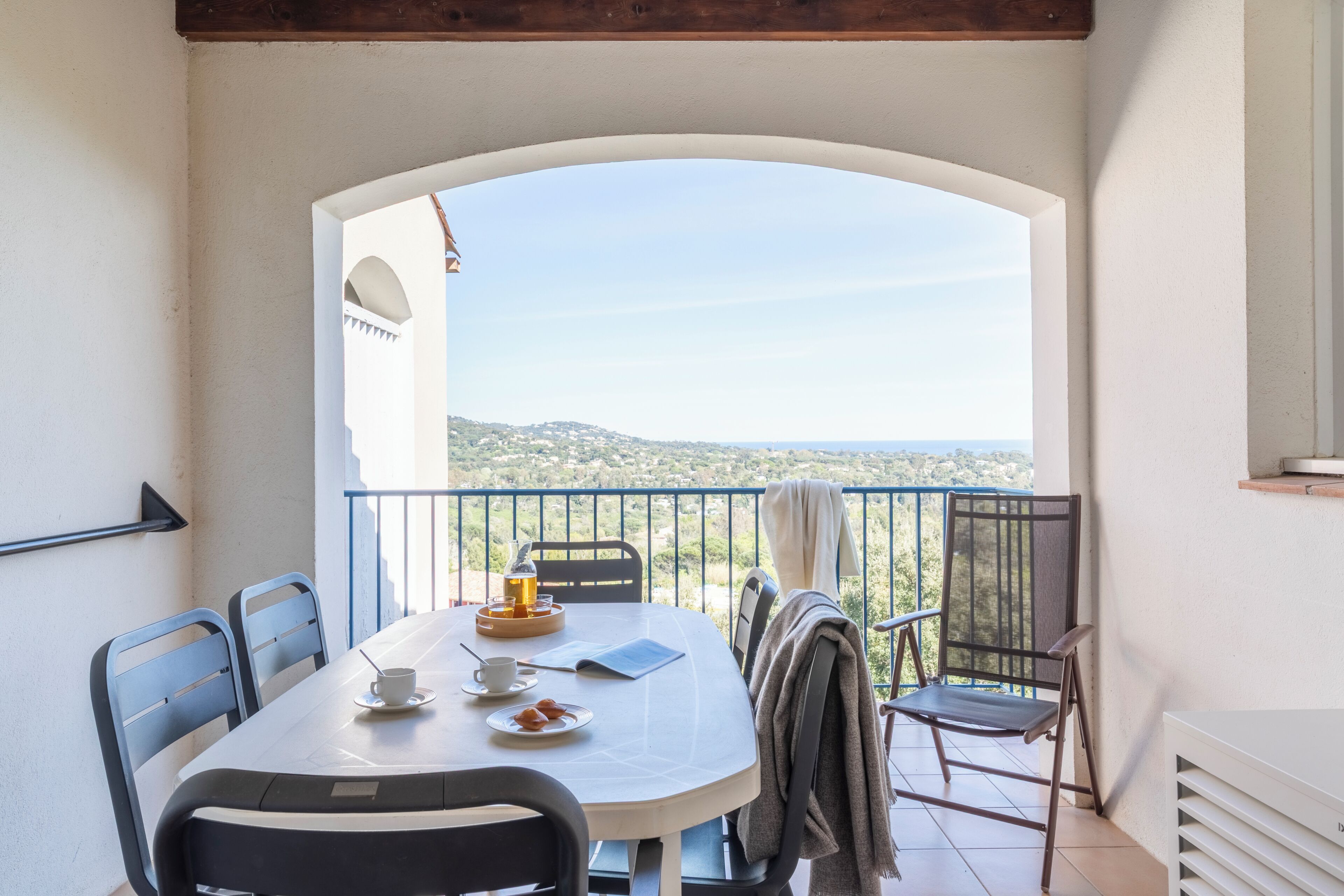 A balcony with a table set for two, chairs, a view of the landscape, and a railing.