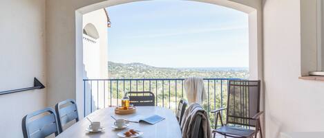 A balcony with a table set for two, chairs, a view of the landscape, and a railing.