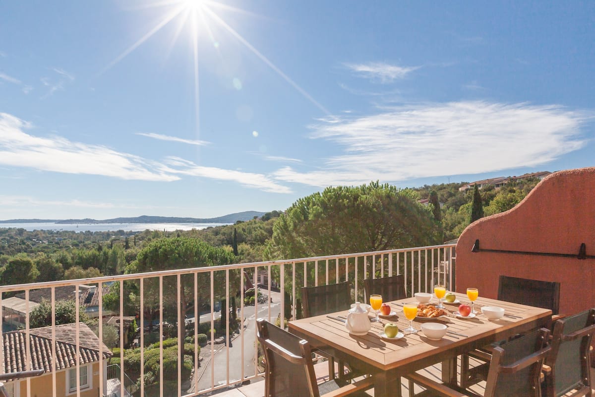 A balcony with a table set for breakfast, overlooking a scenic landscape with trees and hills.