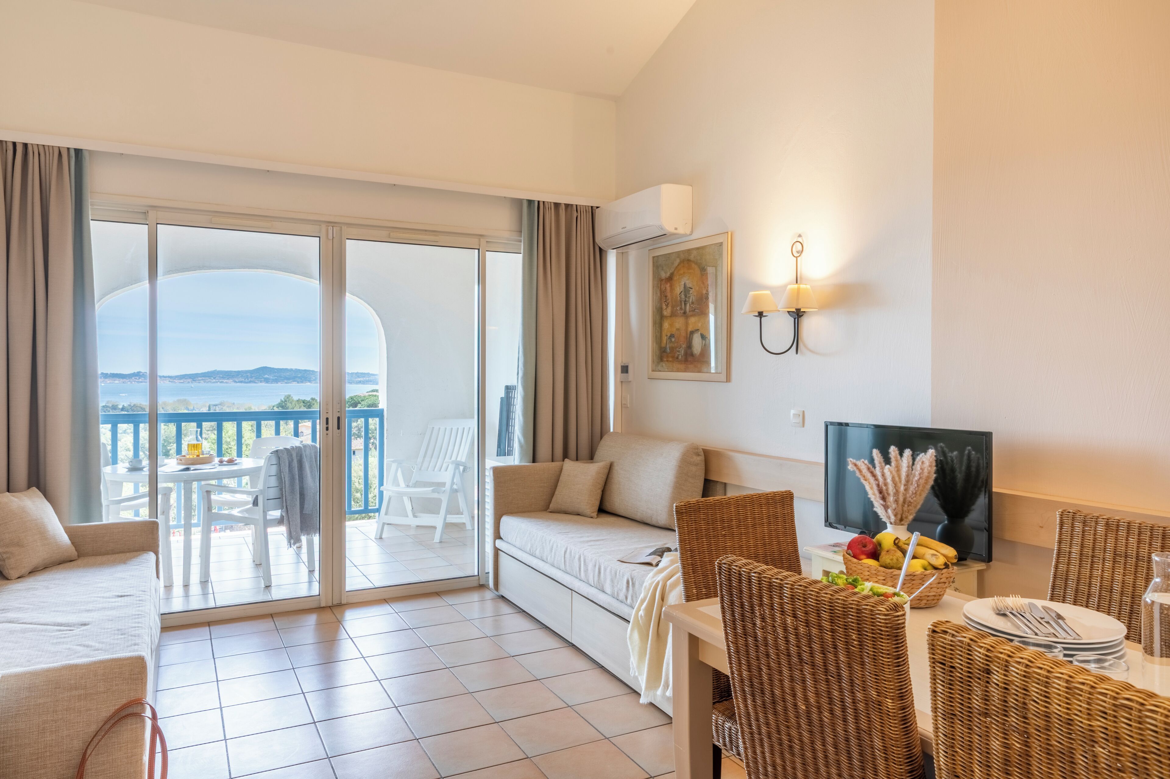 Une chambre d’hôtel avec un balcon, un canapé, une table à manger avec des chaises, une télévision et un tableau au mur.