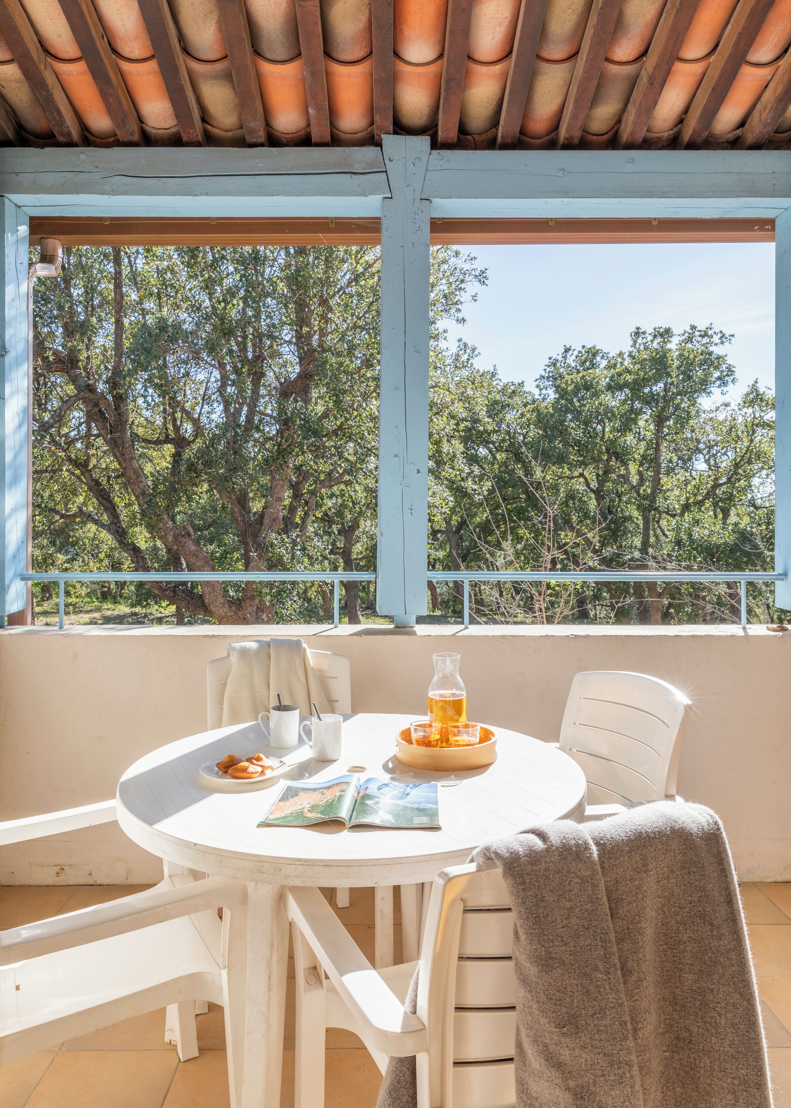 Un balcon avec une table, des chaises, une boisson et un magazine.