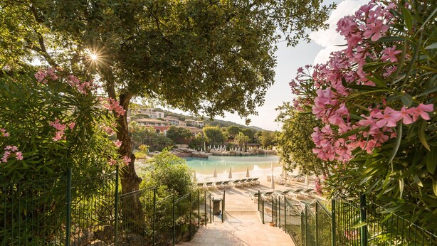 A pathway leading to a pool area with a view of a building and trees.