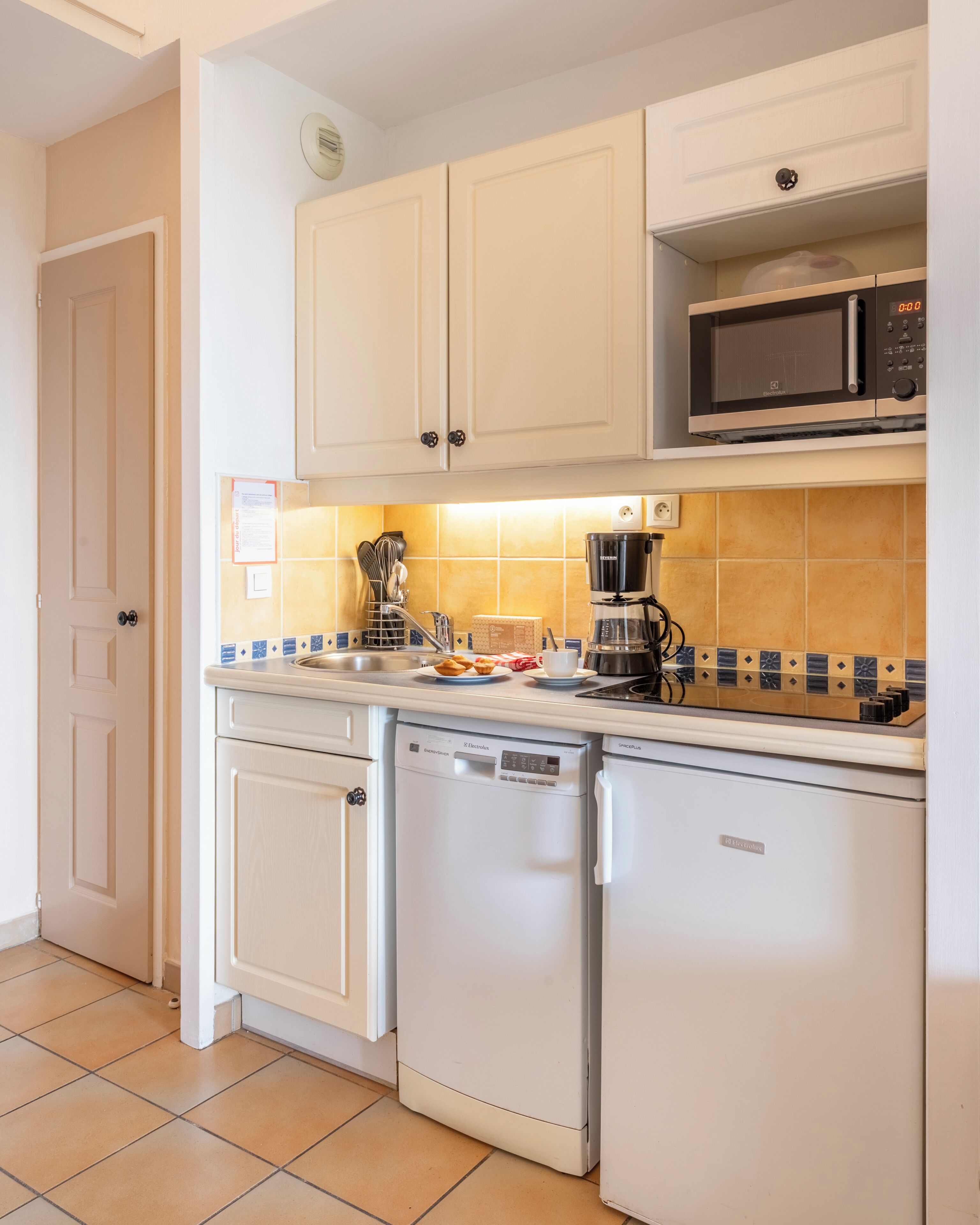 A compact kitchen with white cabinetry, a microwave, a coffee maker, and a dishwasher.
