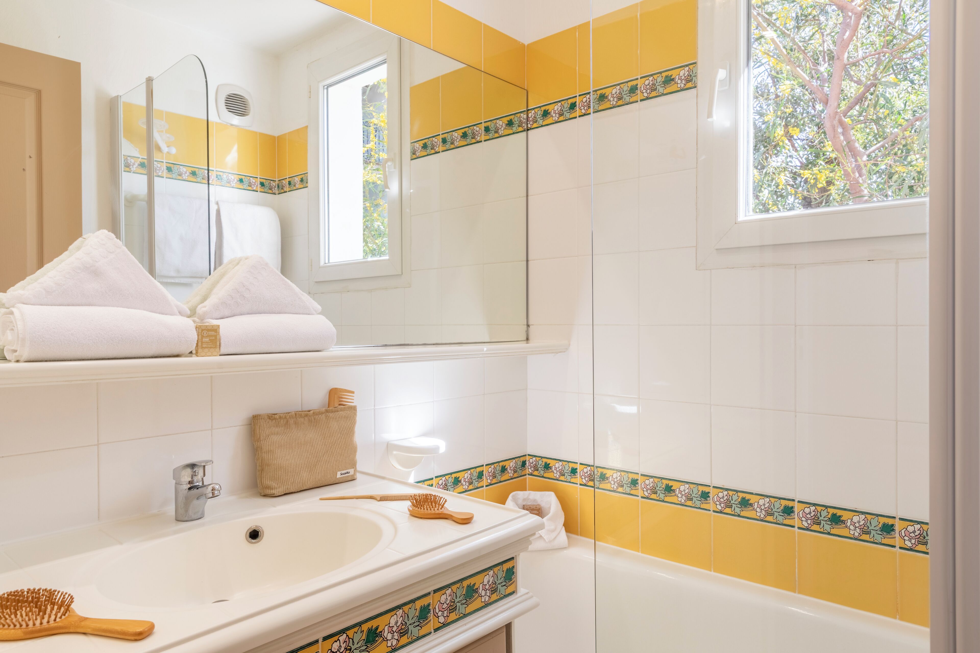 Une salle de bain avec une baignoire, un lavabo, un miroir et une fenêtre.