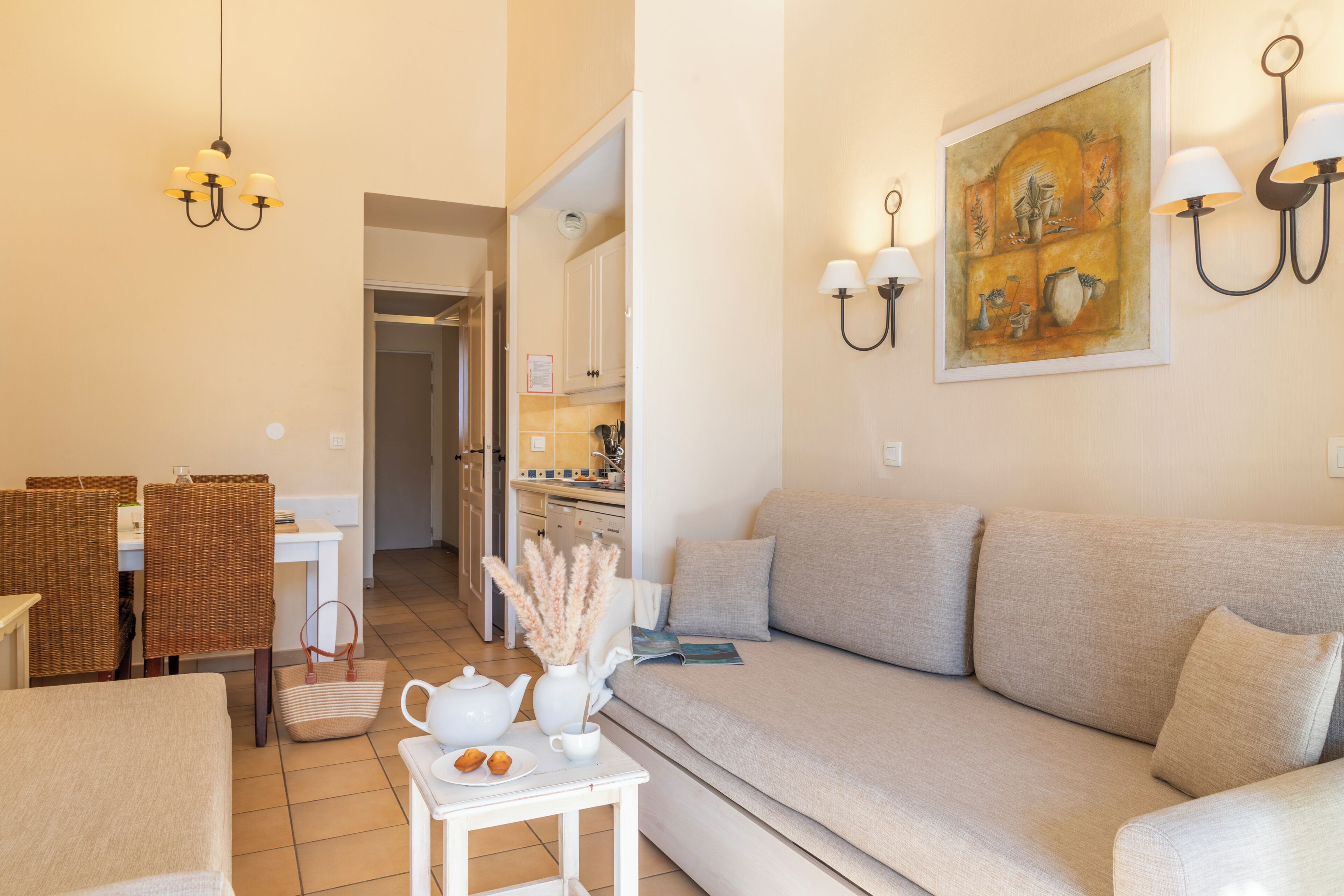 A living room with a sofa, a dining table with chairs, a kitchen area, and a painting on the wall.