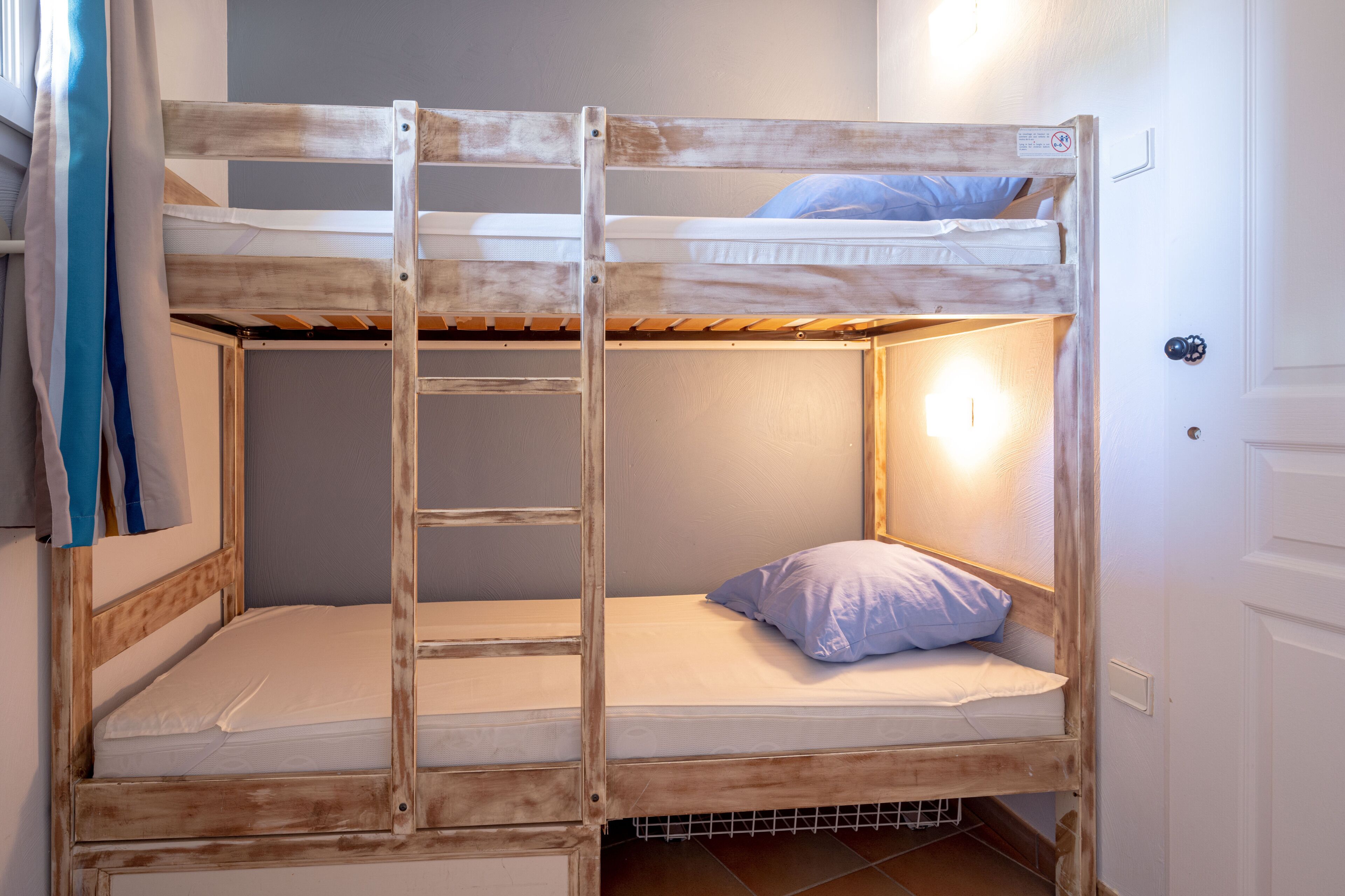 A bunk bed with a ladder, a pillow, and a light source on the wall.
