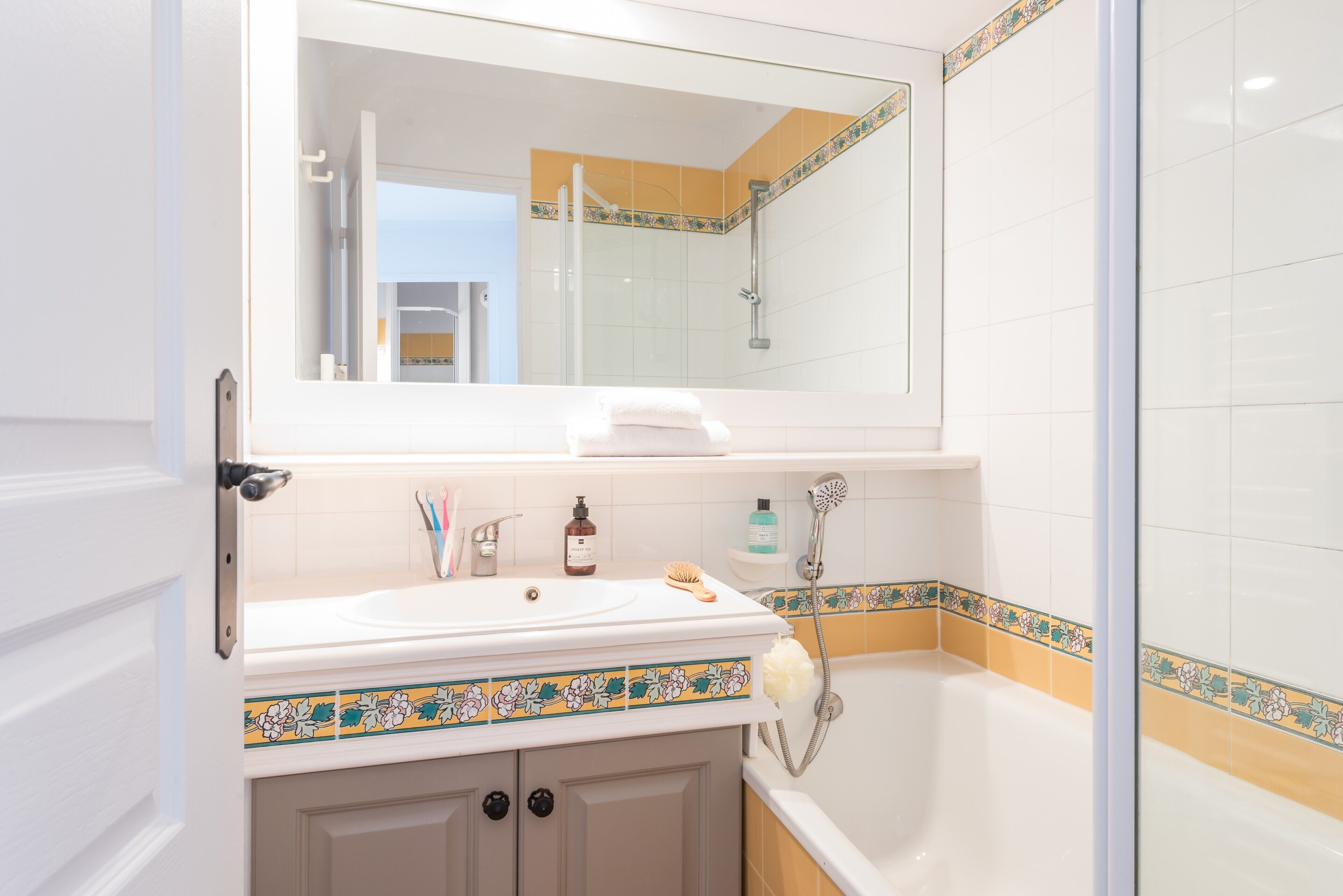 Un bagno con un lavandino bianco, uno specchio, una doccia e un pavimento piastrellato.