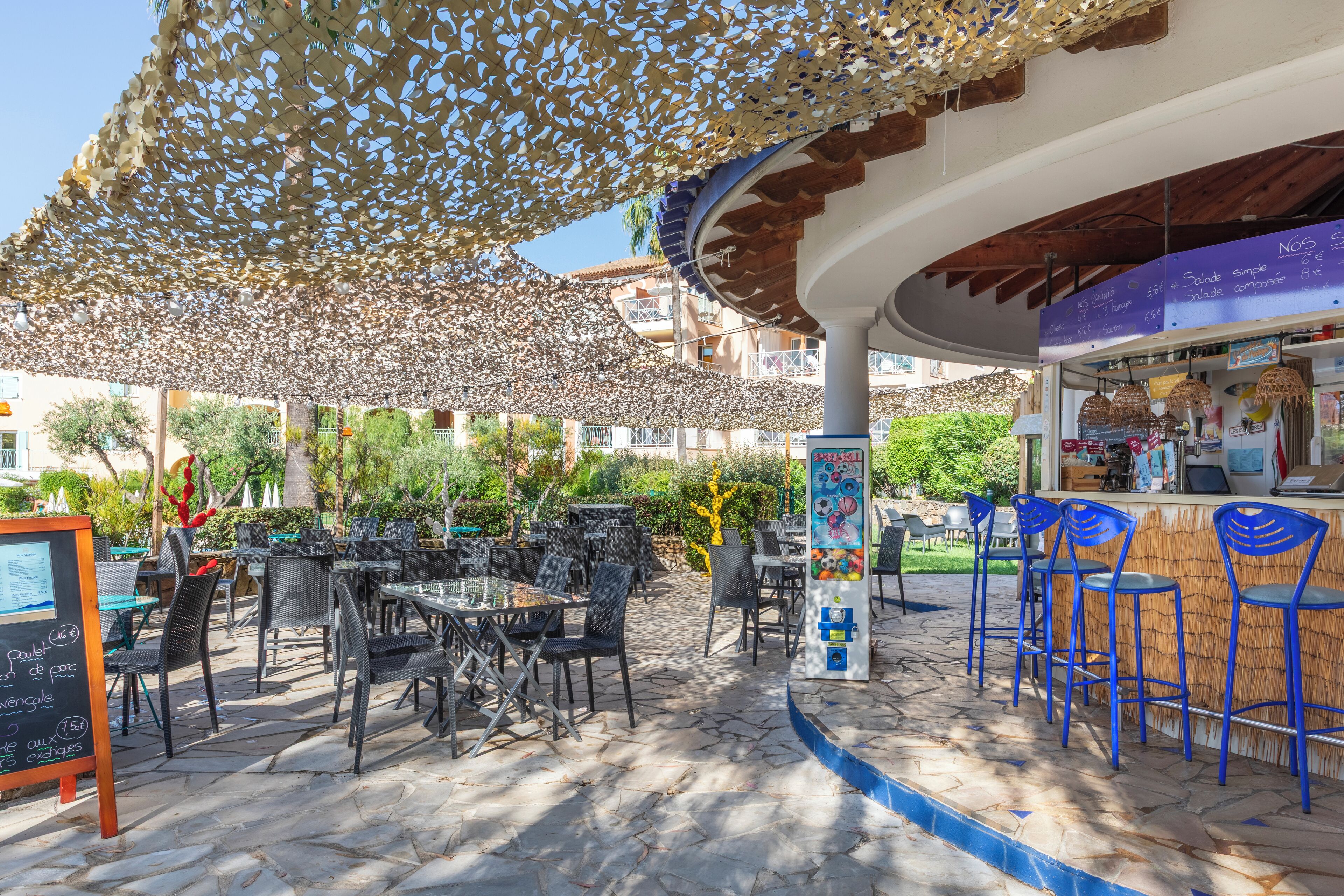 Un café al aire libre con mesas, sillas, una barra y una pizarra con el menú.