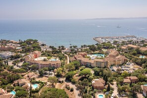 An aerial view of a coastal resort with multiple buildings, swimming pools, and a marina.