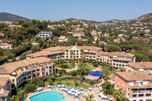 A resort with a swimming pool, multiple buildings, and a hilly backdrop.
