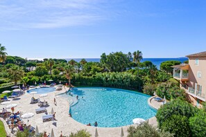 A large outdoor swimming pool surrounded by lounge chairs and umbrellas, with a view of the sea and lush greenery. - Pierre & Vacances Les Rivages des Issambres (Roquebrune-sur-Argens)