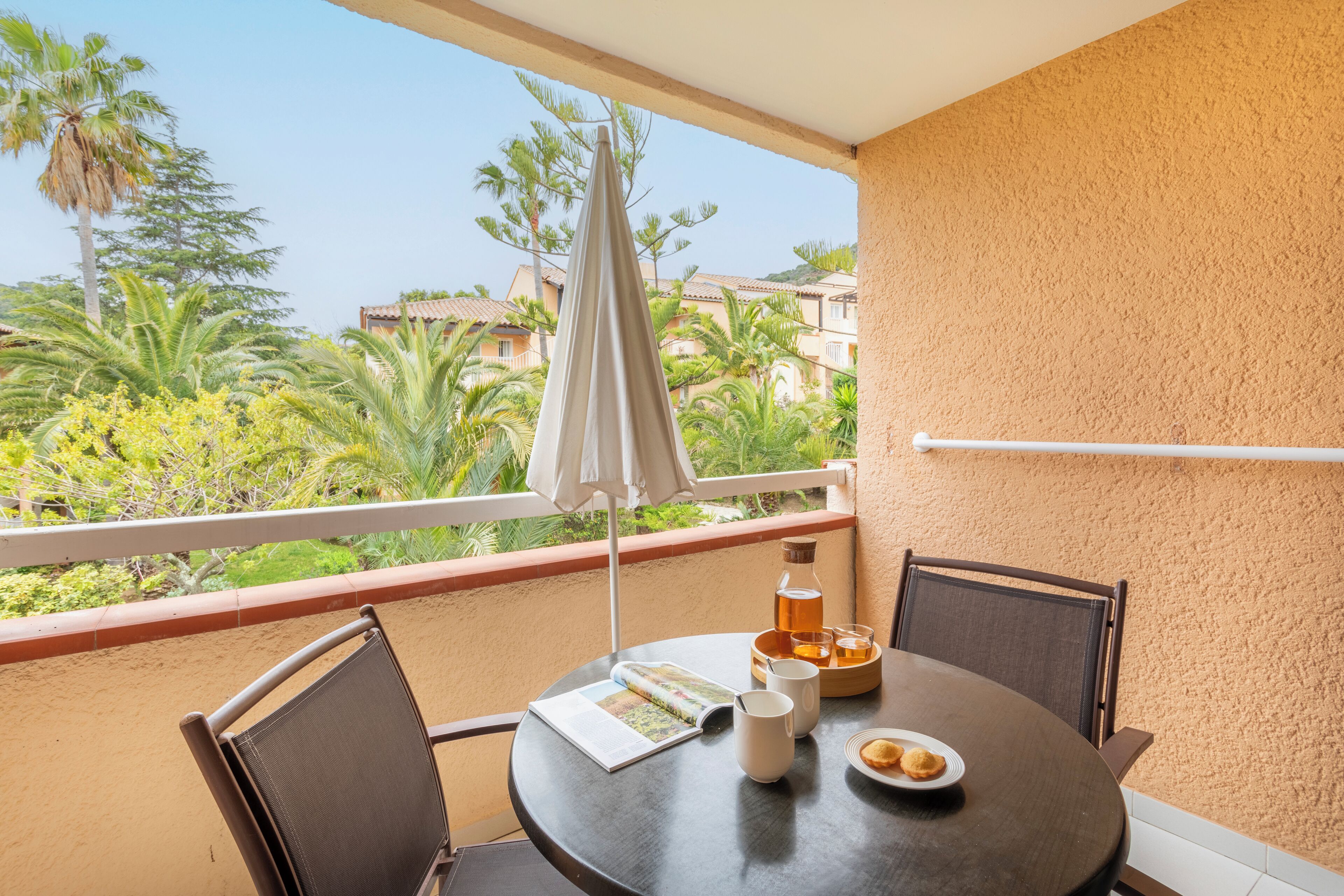 A balcony with a table, chairs, a book, a pitcher, glasses, and a plate of food.