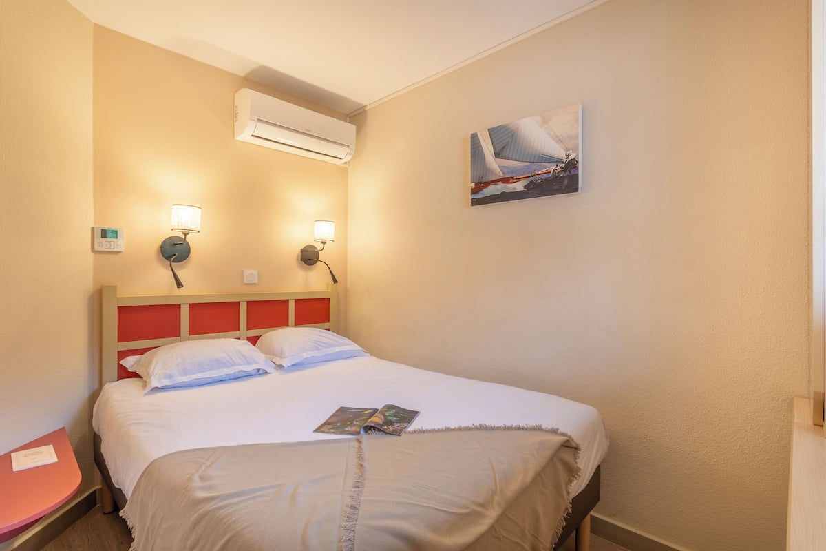 Ein Hotelzimmer mit einem Bett, zwei Wandlampen, einer Klimaanlage und einem Bild an der Wand.