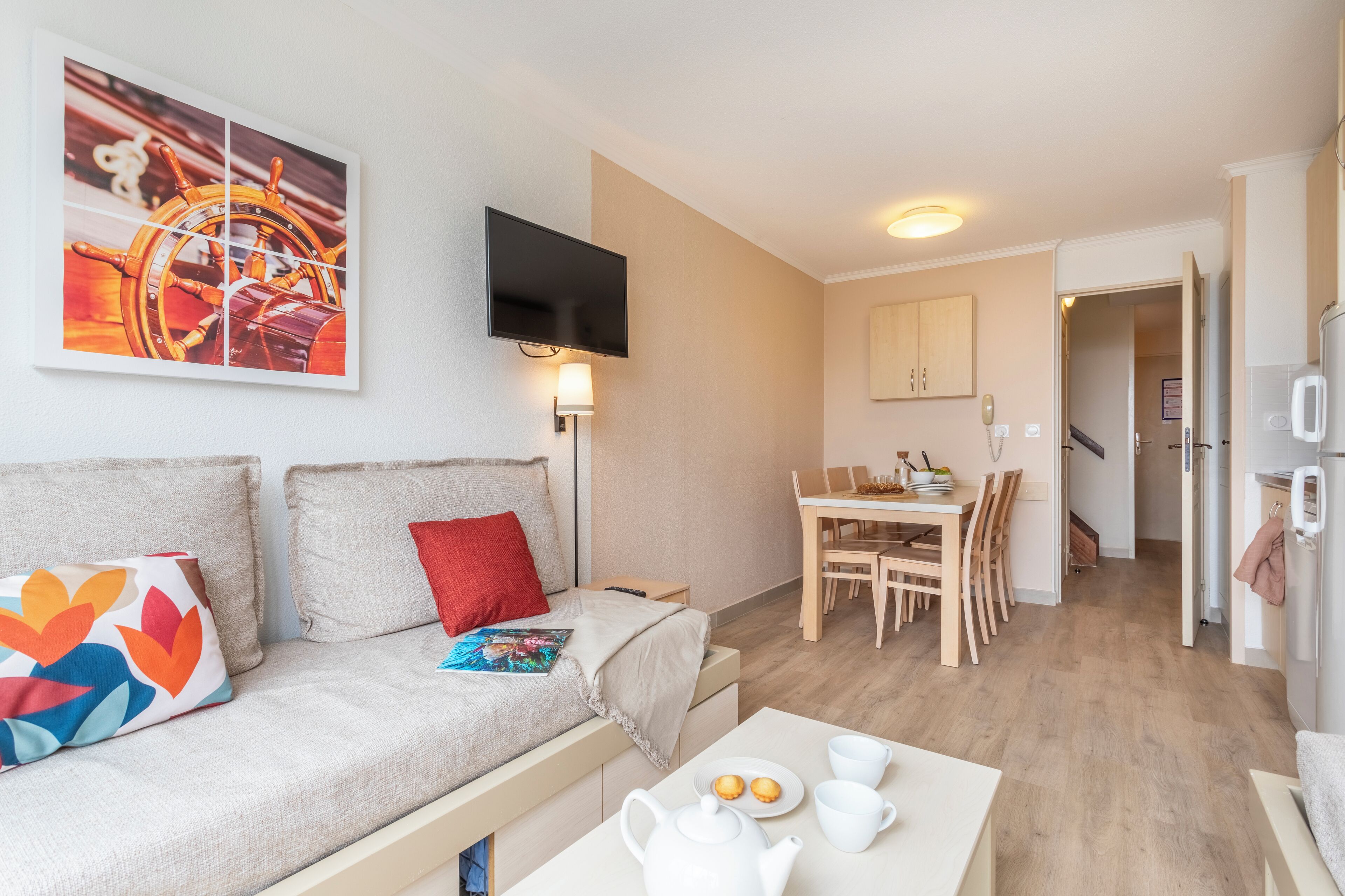 Una sala de estar moderna con un sofá, una mesa de comedor con sillas, una zona de cocina y un televisor montado en la pared.