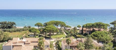 A coastal residential area with Mediterranean-style buildings, a clear view of the sea, and lush greenery.