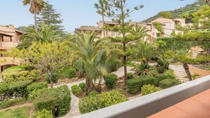A courtyard with palm trees, a stone pathway, and buildings with balconies. - Pierre & Vacances Residence L'Anse de Pramousquier (Le Lavandou)