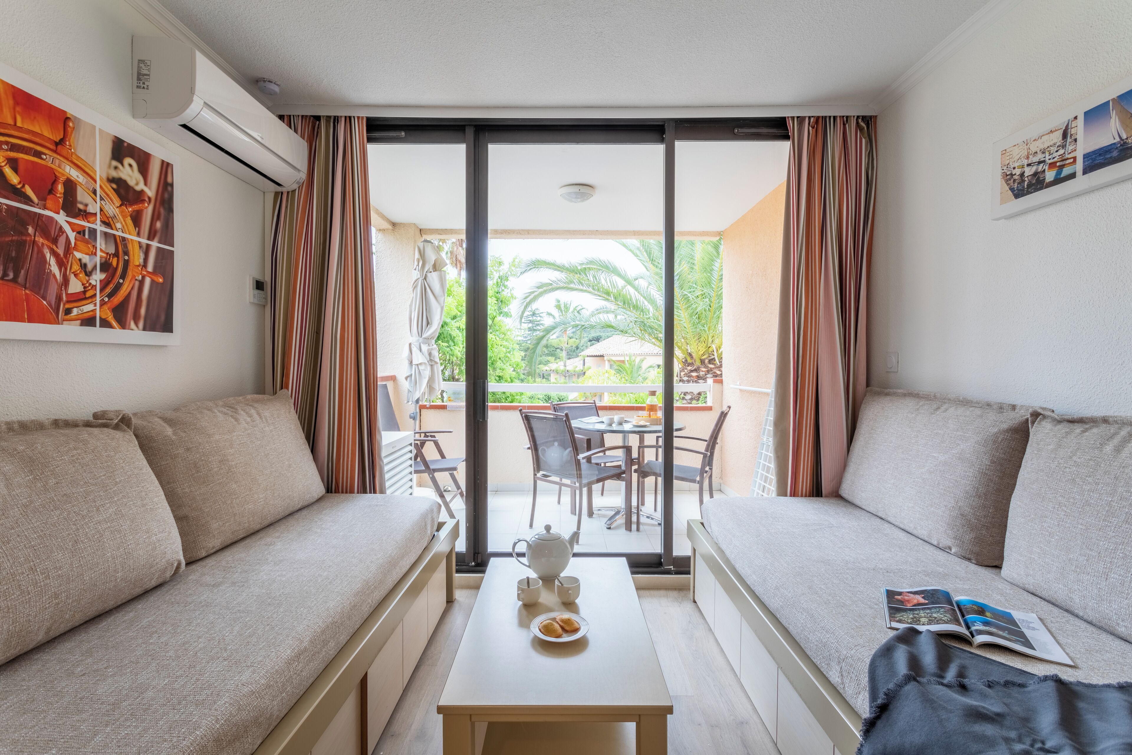 A modern room with a sofa, a small table with a teapot and cups, and a balcony with a table and chairs.