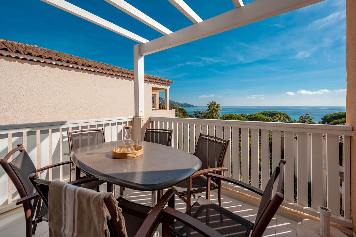 Ein Balkon mit Tisch und Stühlen, der Blick auf die Küste freigibt.