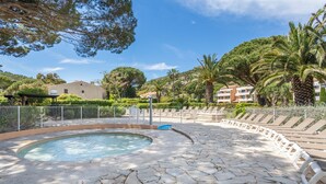 A pool area with a stone floor, lounge chairs, and a building in the background. - Pierre & Vacances Residence L'Anse de Pramousquier (Le Lavandou)