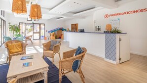 A modern hotel reception area with wicker furniture, a reception desk, and a view of the outdoor area. - Pierre & Vacances Residence L'Anse de Pramousquier (Le Lavandou)