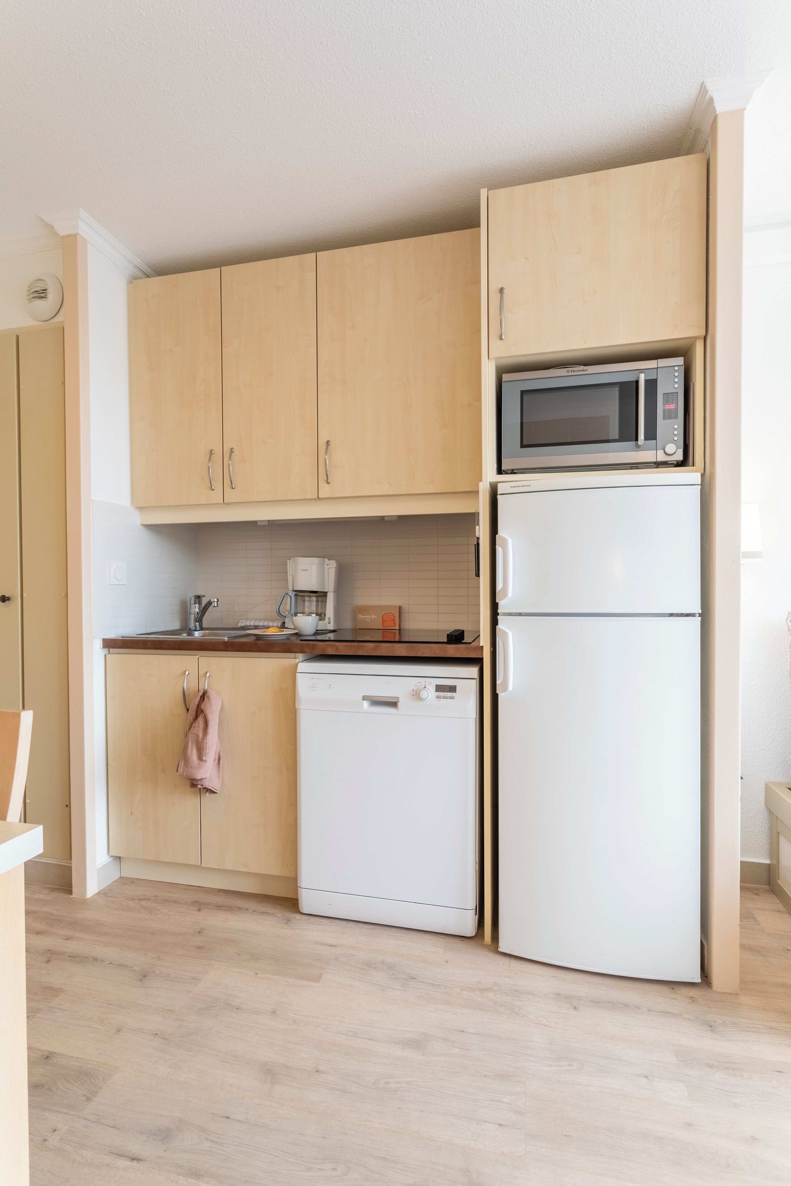Una cucina compatta con mobili in legno, un forno a microonde, un frigorifero bianco e una lavastoviglie.
