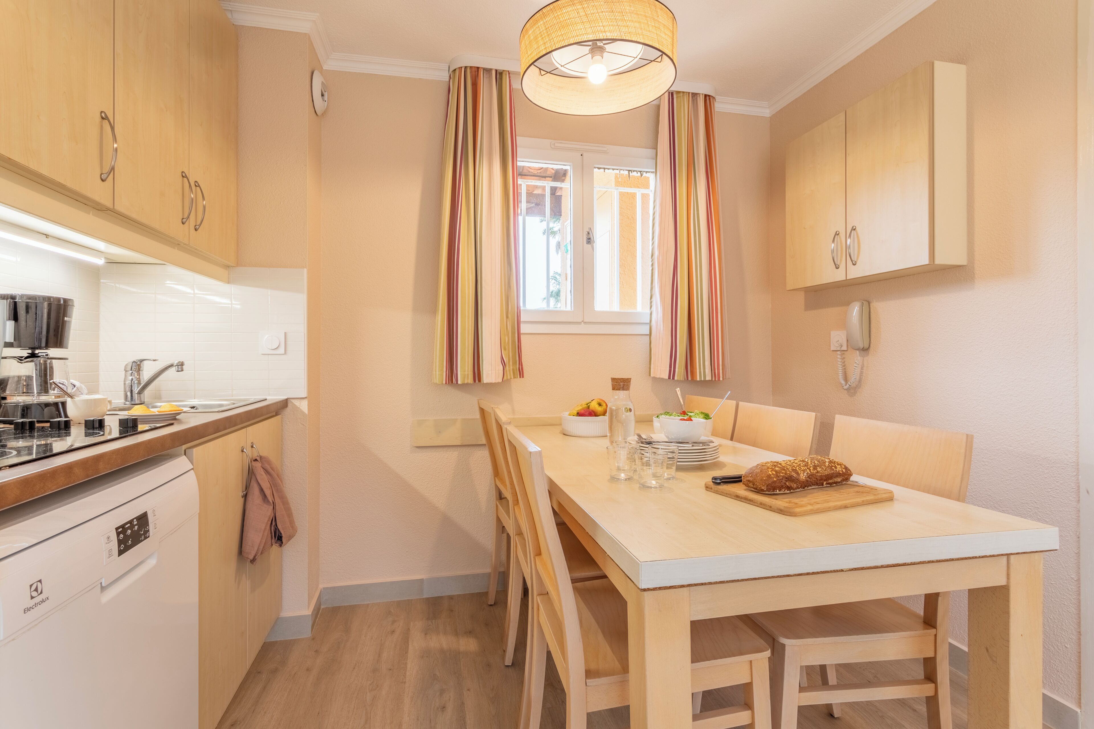A modern kitchen with wooden cabinets, a white countertop, and a dining area with a table and chairs.