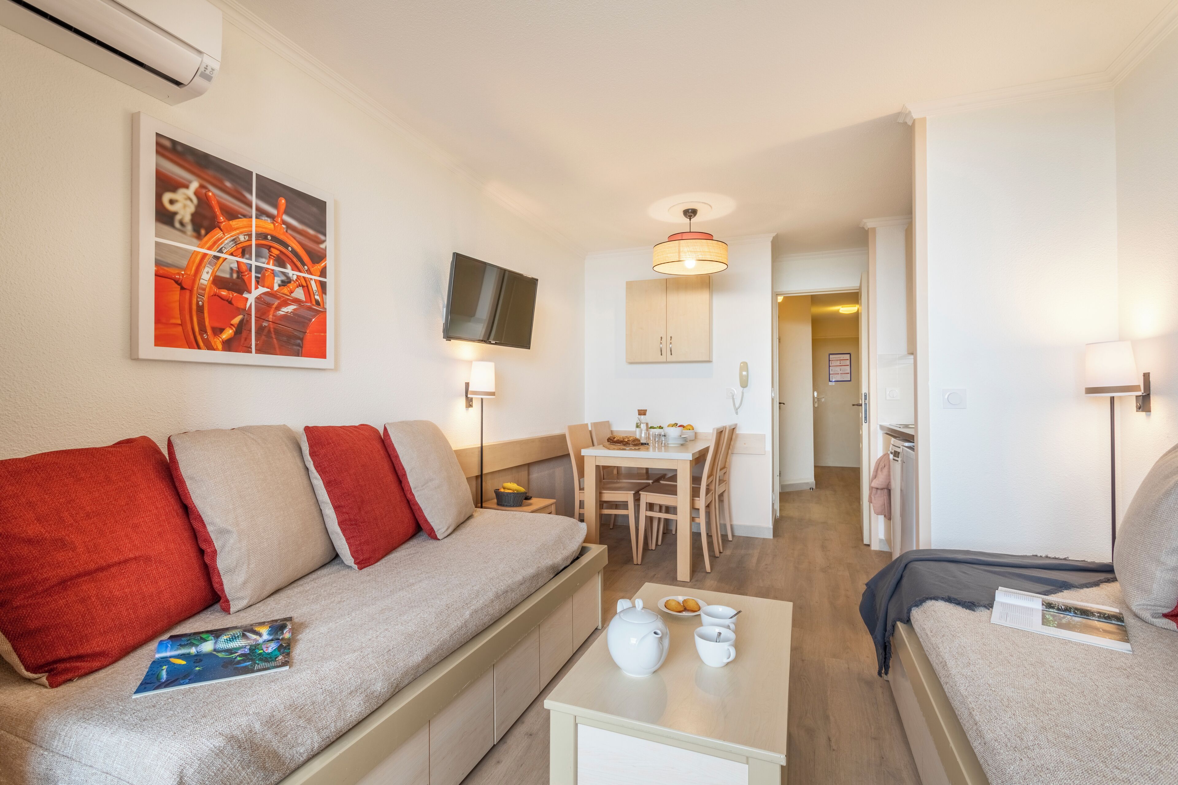 Una habitación de hotel moderna con sofá, una mesa de comedor y un televisor montado en la pared.