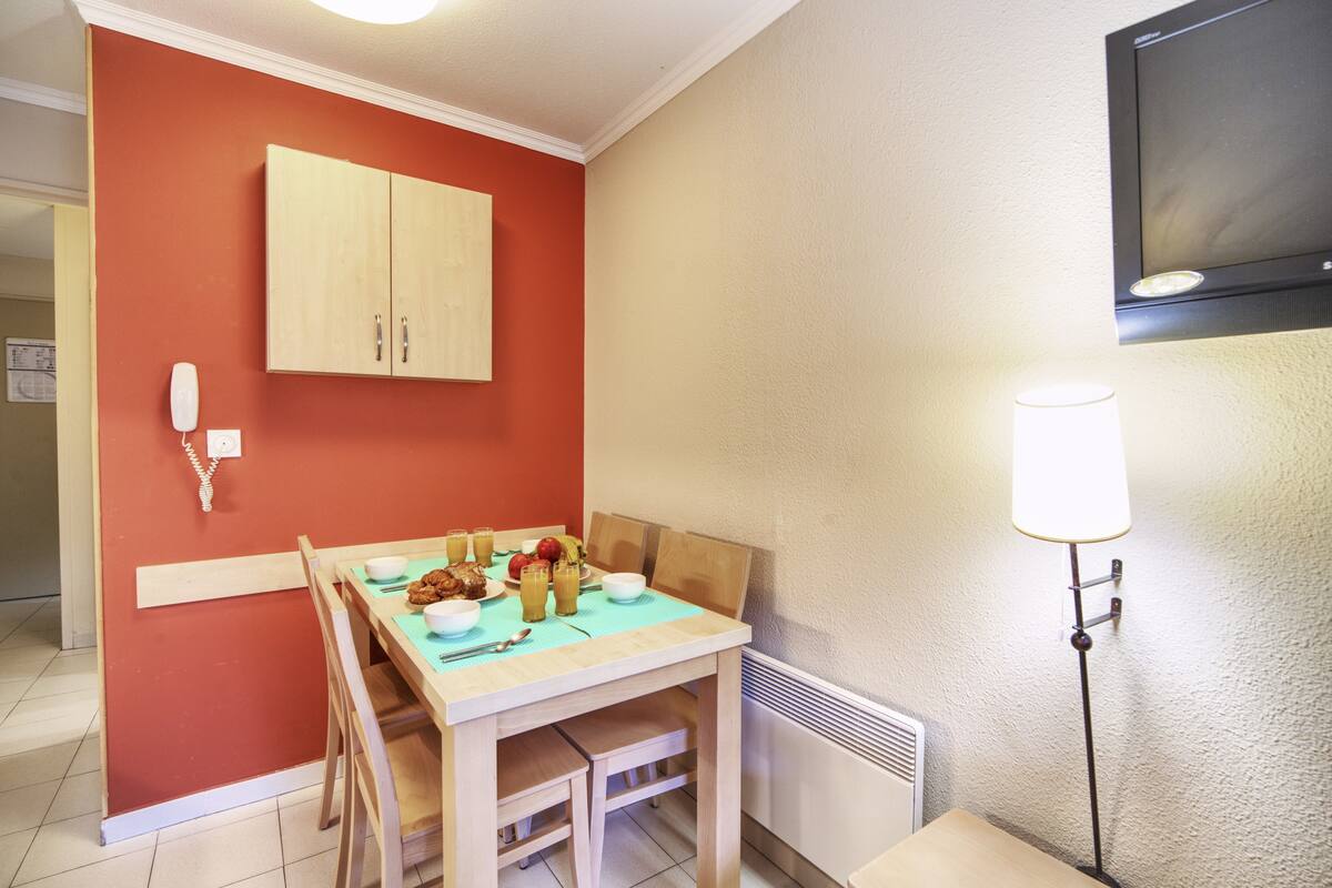 Ein Essbereich mit einem Holztisch, gedeckt für zwei Personen, einer roten Wand, einer weißen Decke und einer Stehlampe.
