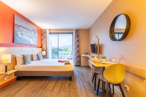 Une chambre d’hôtel équipée d’un lit, d’un bureau, d’une chaise, d’une télévision et d’une grande fenêtre donnant sur un beau paysage.