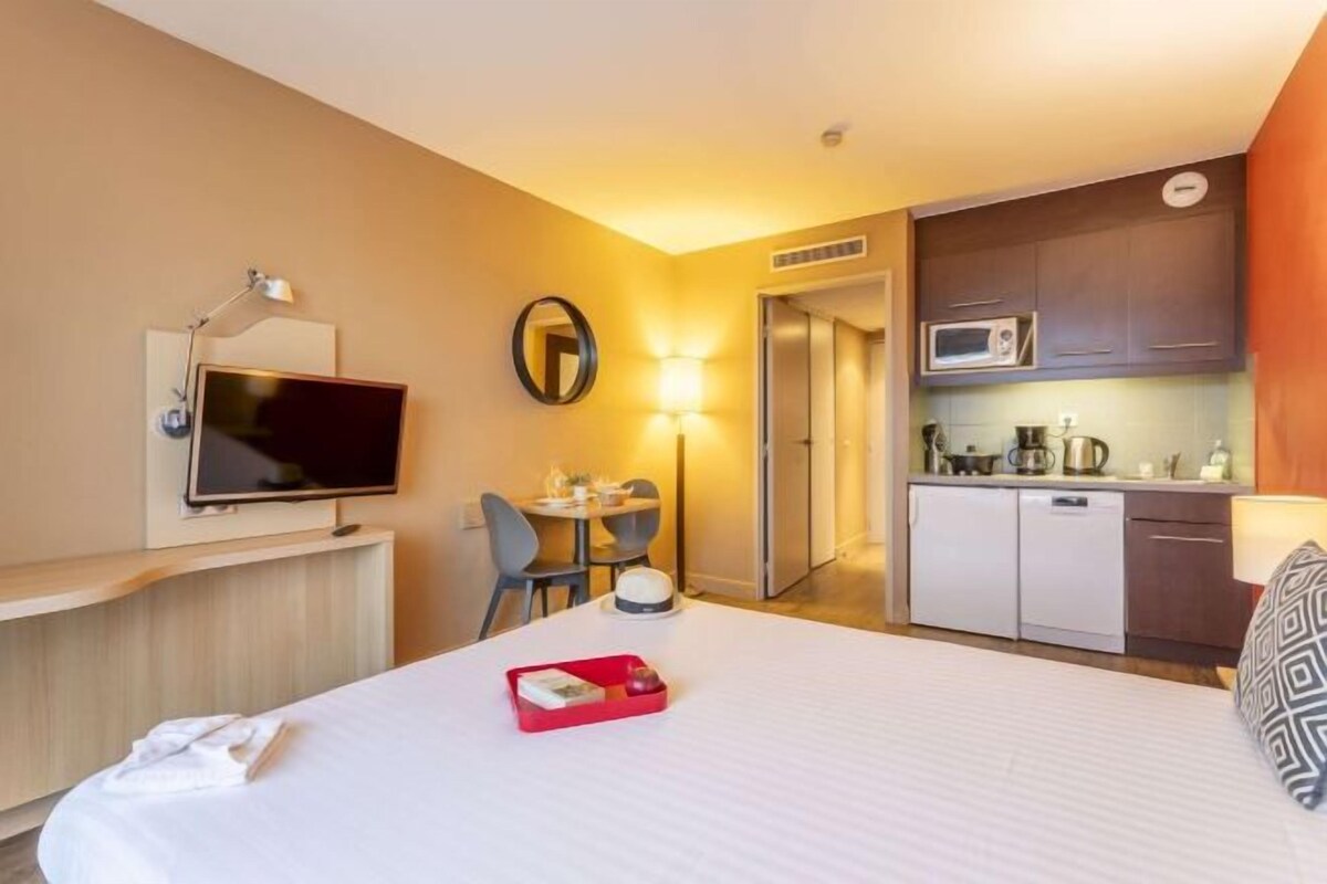 Habitación de hotel con cama, escritorio con televisor, zona de comedor y kitchenette.