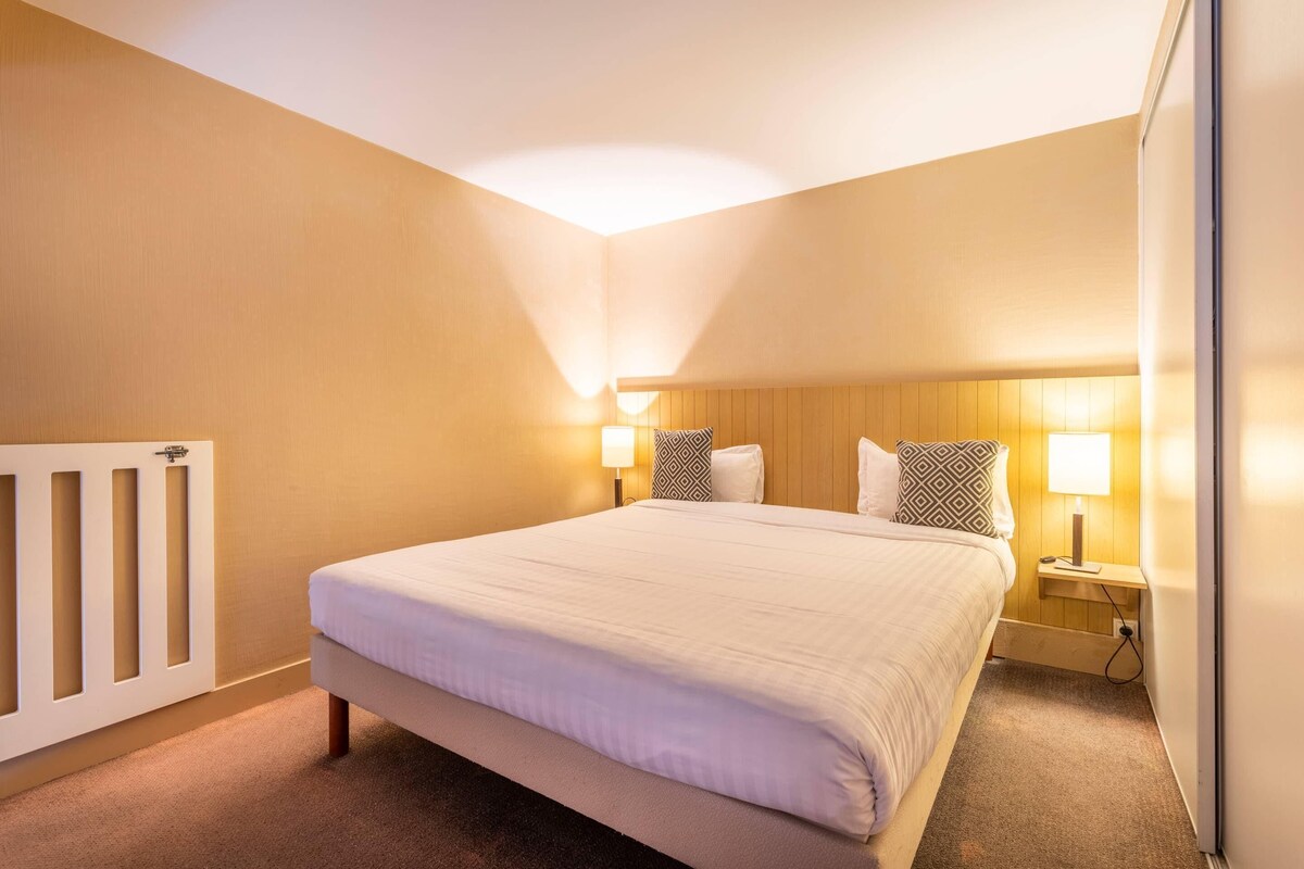 Een hotelkamer met een groot bed, twee bedlampen, een houten hoofdeinde en een witte radiator.