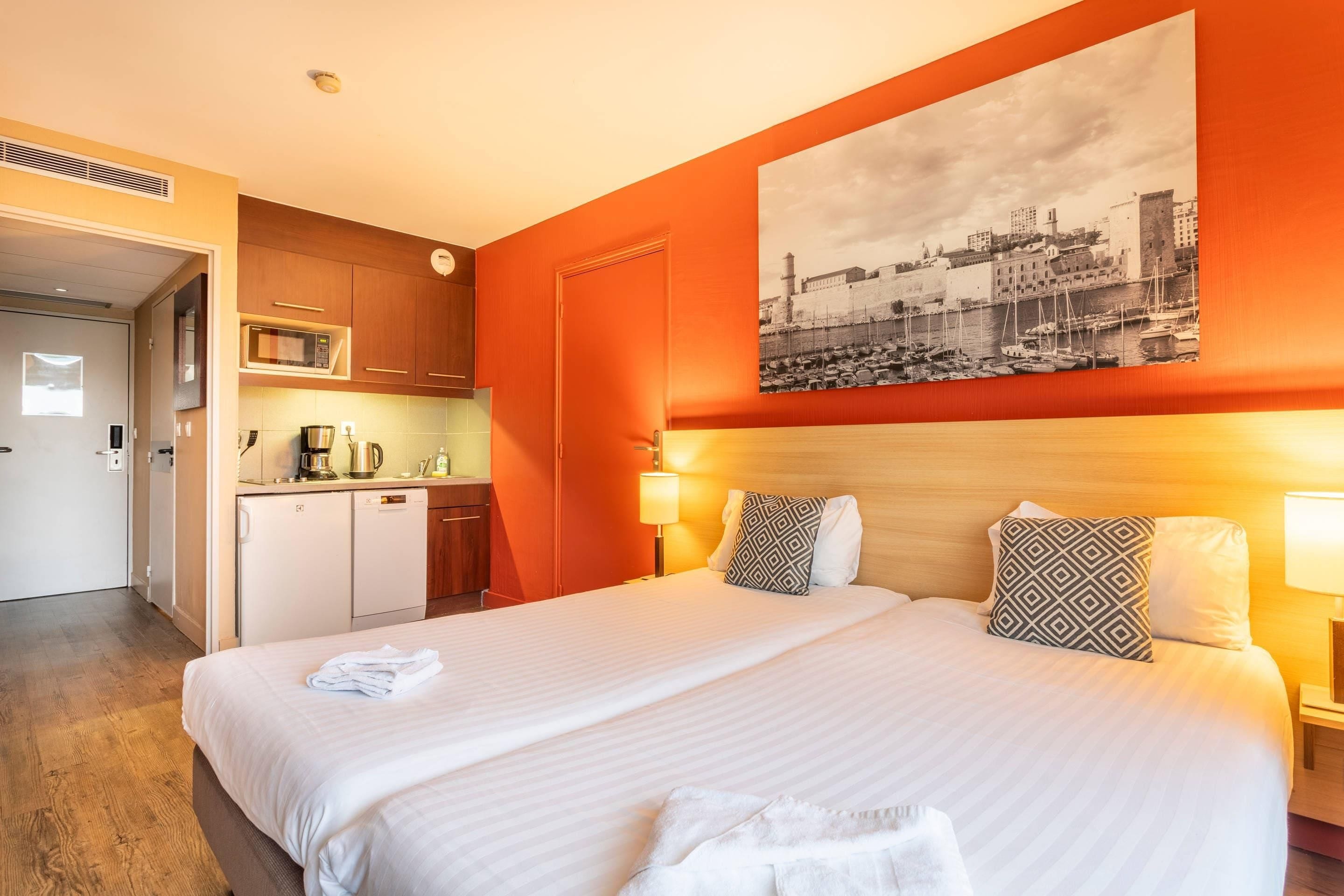 Habitación de hotel con cama, una zona de cocina y un cuadro de paisaje urbano en la pared.