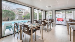 A modern dining area with tables and chairs, large windows, and a view of a swimming pool.