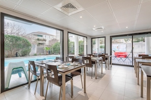 Un espace repas moderne, doté de tables et de chaises, de grandes fenêtres et offrant une vue sur une piscine.
