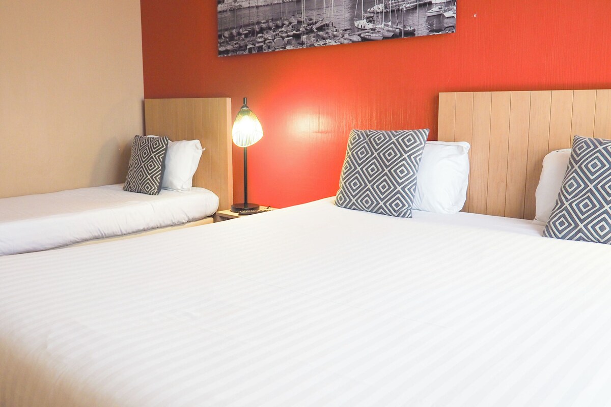 Une chambre d’hôtel avec deux lits simples, une table de chevet avec une lampe et un tableau accroché au mur.